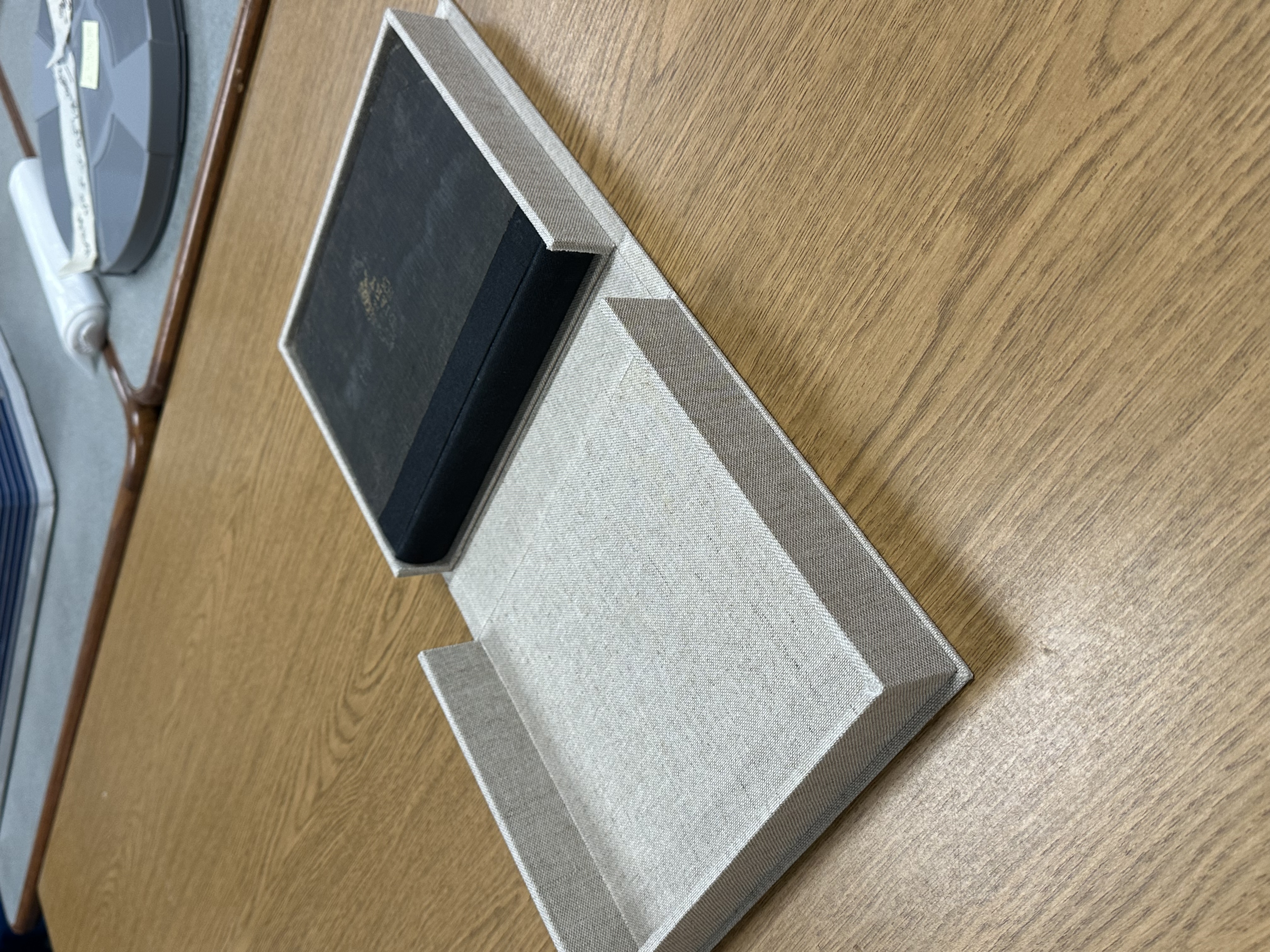 Gray clamshell box with a black book inside, fully open and lying flat on a table.
