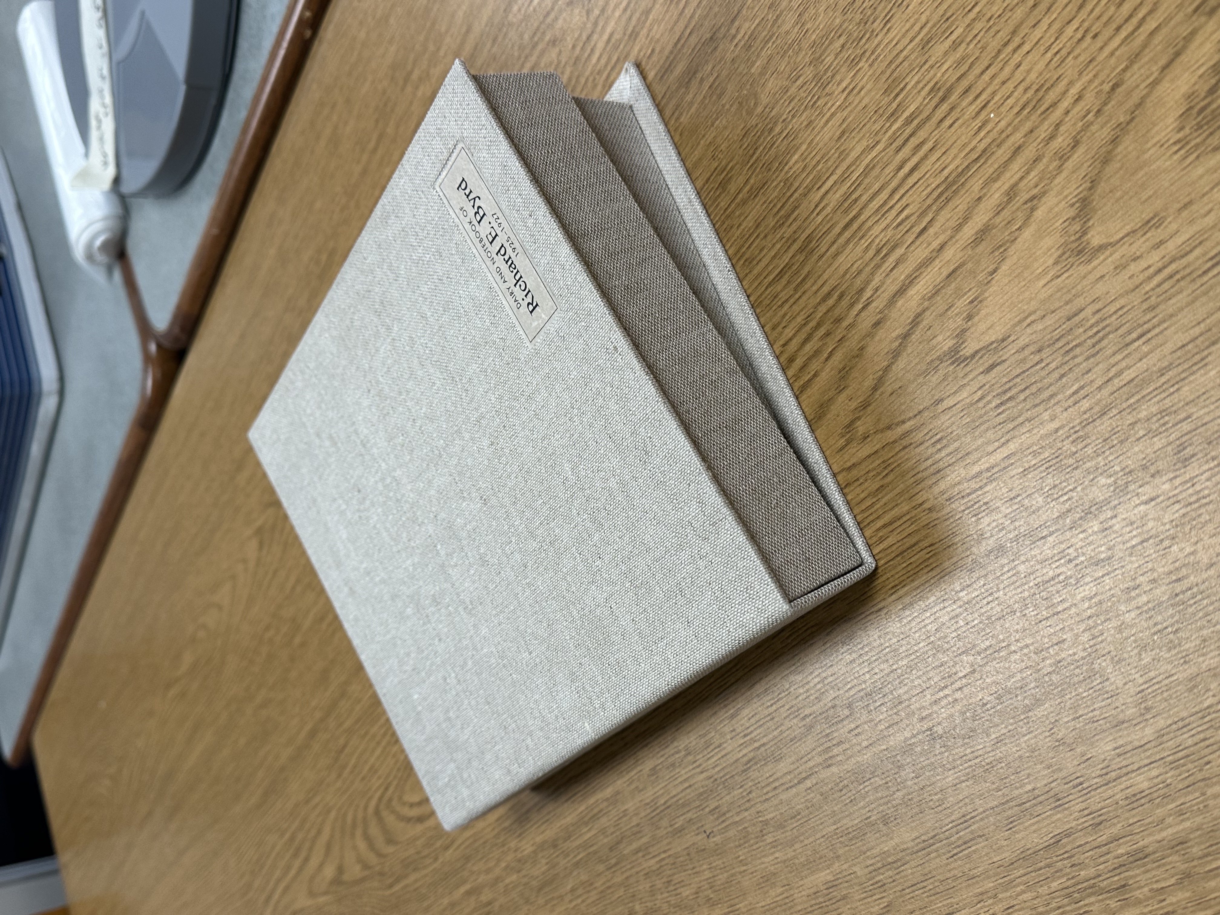 Gray clamshell box with a black book inside, nearly closed on a table.